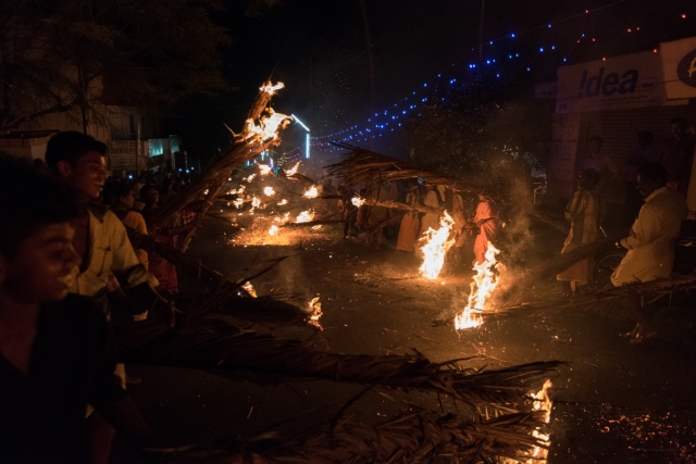Villagers burning dry coconut leaves while welcoming the kolam procession. 